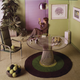 “A smiling short-haired woman in a print dress sits on the floor by the window and admires a bunch of grapes in a green dining room with one chair and a table with a glass top, 1970s.” Via Getty.